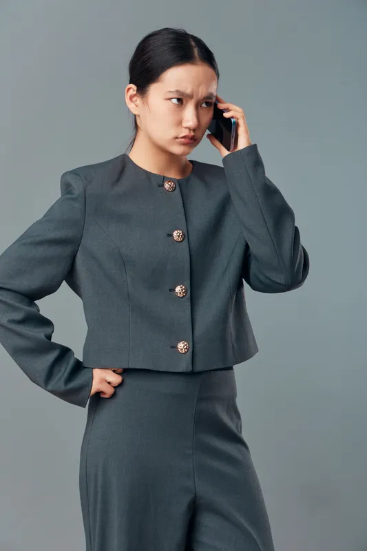 Businesswoman in gray suit with serious expression talking on phone, standing with hand on hip against plain background for professional communication and work concept.