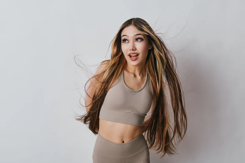 Young woman with long hair wearing sportswear posing and looking away on neutral background, fitness lifestyle, beauty and health concept with movement.
