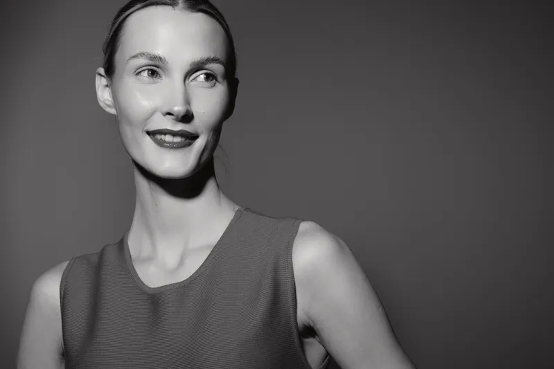 Portrait of a young Caucasian woman with fair skin and pulled back hair smiling confidently in studio lighting on plain background. Concept of beauty, elegance, and positive mood.