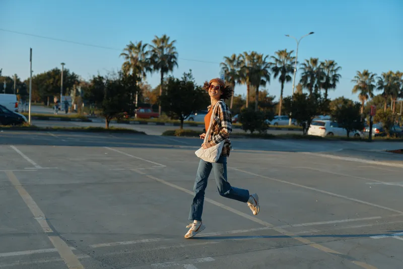 woman jump in empty parking under palm trees, casual outfit and joyful motion in warm sunlight, candid lifestyle moment of authenticity, golden hour glow, mindful living and emotional storytelling.