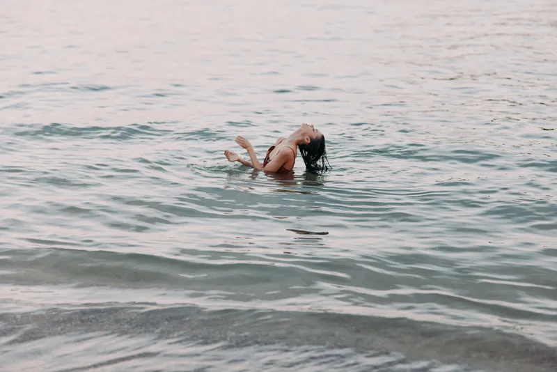 A solitary figure floats in calm sea, back arched and hair spilling over the surface, capturing a moment of serenity and freedom beneath soft light.