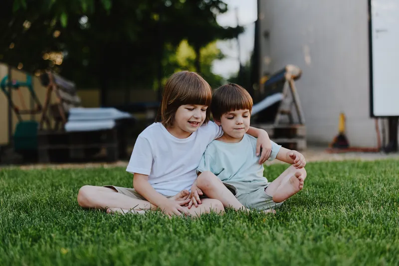 Happy children sitting together on grass, enjoying a sunny day in the park, sharing laughter and playful moments with friends outside.