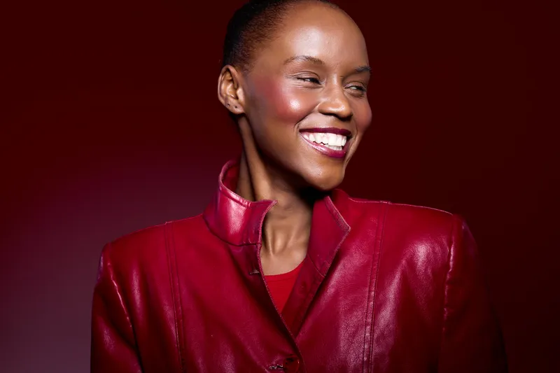 Portrait of a smiling African woman with dark skin wearing a red leather jacket against a red background. Concept of beauty, fashion, confidence, and vibrant style.
