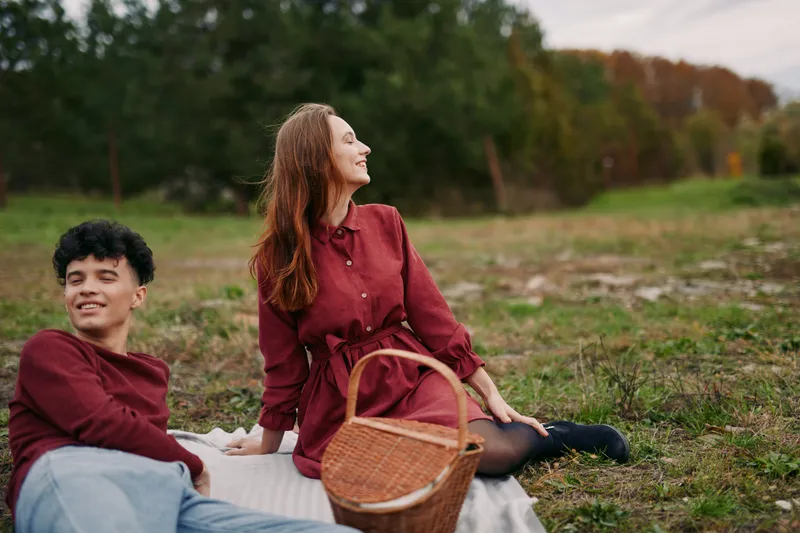 Young couple enjoying a relaxed outdoor picnic on a blanket in a grassy field, captured with authentic natural expressions and candid interaction that convey genuine connection and warmth.