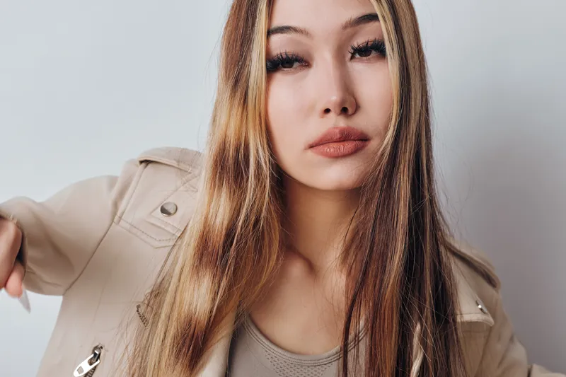 Young woman with long straight hair wearing beige jacket and neutral makeup posing against plain background. Fashion, beauty, model, lifestyle and portrait focus with confident expression.