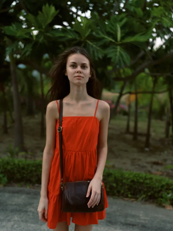 Young woman in red dress standing outdoors near trees, with natural greenery and soft evening light creating a calm mood.