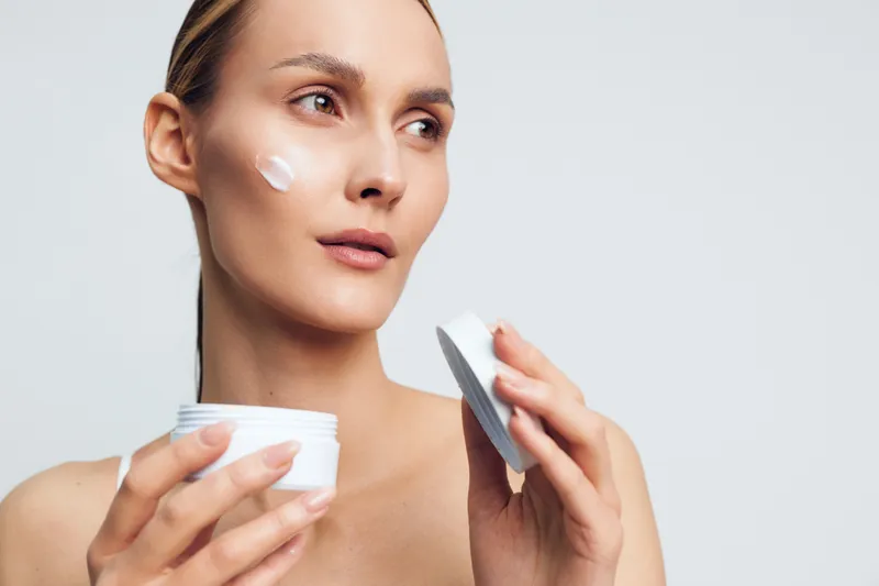 Young woman skincare routine, applying face cream with cotton pad, visible hydration on smooth skin, beauty and cosmetics care, hygiene self grooming, closeup portrait on light background.