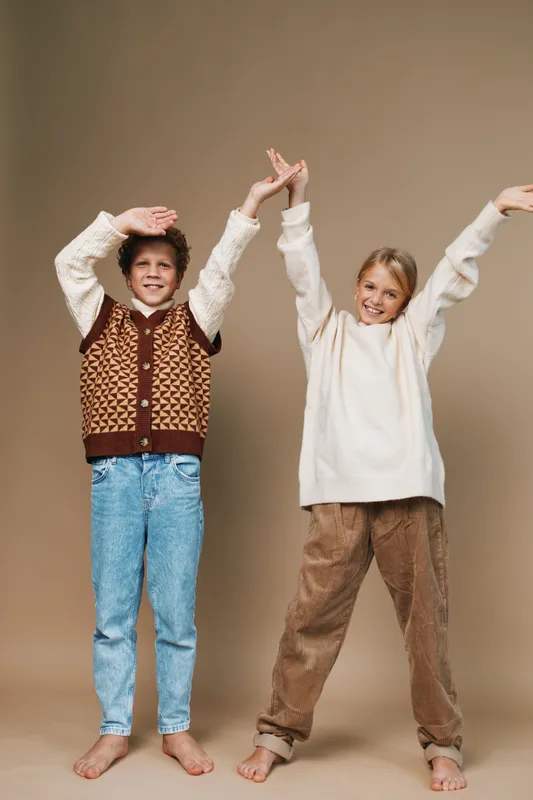 Authentic scene of two children in casual school style, arms raised in cheerful play, capturing a candid lifestyle moment with warm, friendly energy.