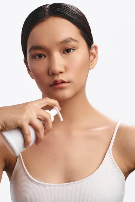 Asian woman applies skincare product in a clean, minimal setting. She looks calm and focused, presenting a fresh, modern beauty routine moment.