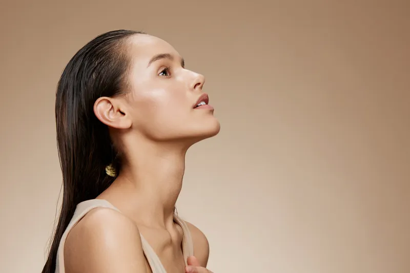 Elegant profile portrait of a young woman with long, straight hair and natural makeup, showcasing a serene expression against a soft beige background