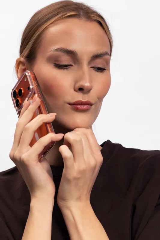 Young woman with closed eyes holds smartphone near face, wearing dark clothes on white background. Concept of communication, technology, and modern lifestyle.