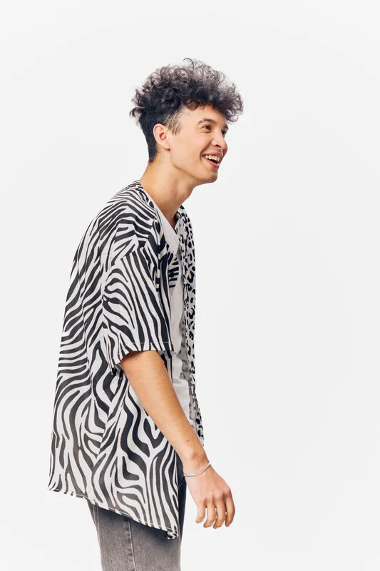young man smiling in zebra print shirt with curly hair standing against white background, casual style and joyful mood captured in portrait