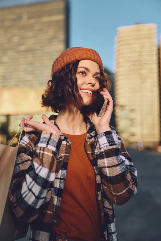 woman smile shopping phone urban candid authenticity captured in a golden hour glow; young female enjoying mindful living and candid lifestyle, emotional storytelling in a warm city street.
