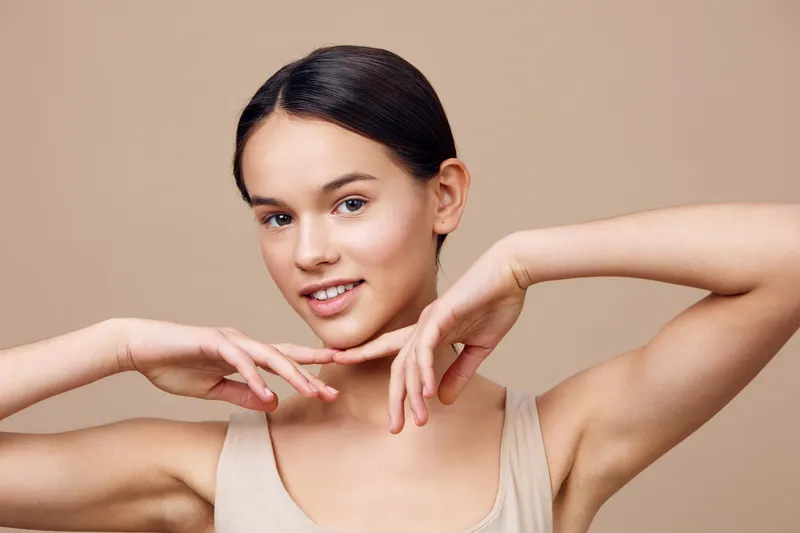 Young woman smiling with a natural expression, showcasing healthy skin in a minimalistic beige background, perfect for beauty and skincare themes
