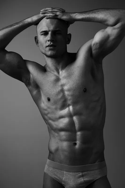 Athletic man posing confidently in a black and white portrait, showcasing his toned physique and strong presence, creating a striking visual impact.