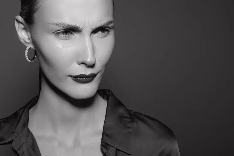Close-up of a white woman with pale skin showing a confused expression. She wears hoop earrings and a dark shirt in a studio with dark background. Concept of doubt and uncertainty.