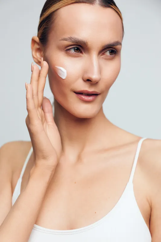 Young woman applying face cream on clean skin, skincare routine, natural beauty, soft lighting, closeup portrait, healthy glowing complexion, minimal makeup, white background