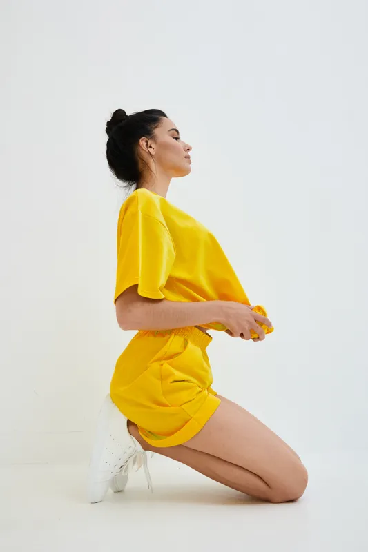woman kneeling in bright yellow casual outfit against white background, styled hair, minimalistic and modern look, youthful and relaxed mood