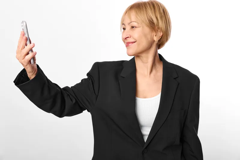Woman holding smartphone, senior business portrait, smiling in black blazer, using digital device for communication, technology and remote contact, studio white background