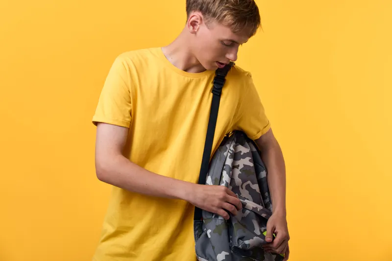Teenager with camouflage backpack on a bright yellow backdrop, casual clothing, preparing for school or commute, vibrant color contrast and everyday style