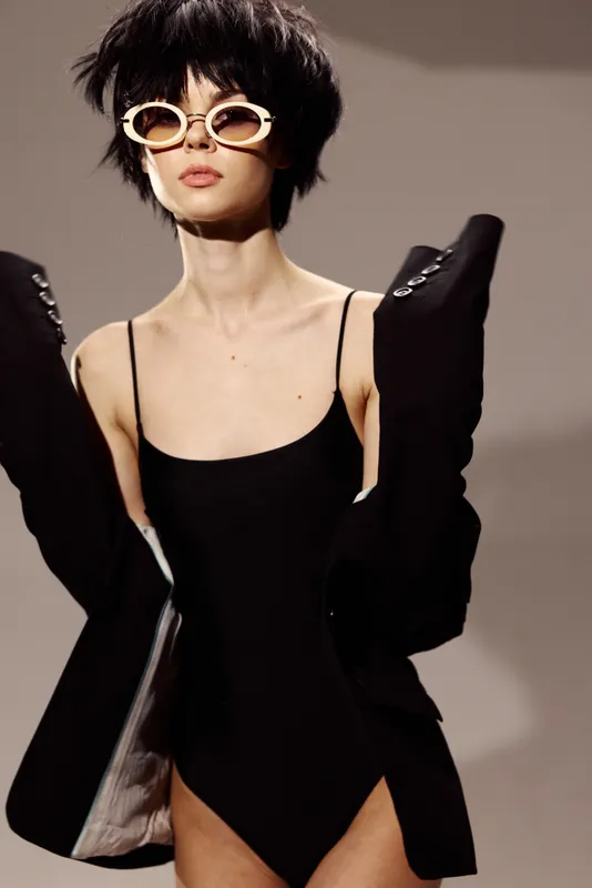 Stylish woman wearing black bodysuit and sunglasses with short hair in minimalistic setting