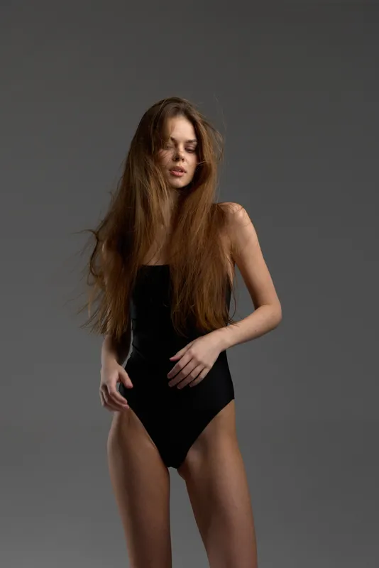 Young woman with long hair wearing black bodysuit standing against grey background