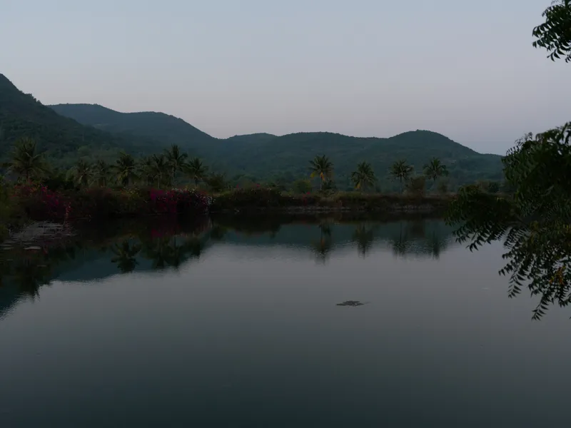 Calm mountain lake at dusk with lush green trees and clear sky, reflecting tranquil nature and serene landscape in peaceful evening light.