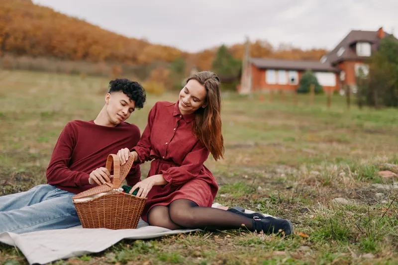 An intimate outdoor picnic scene captures a genuine moment as a young couple share bread in a sunny field, conveying authenticity through natural gestures.