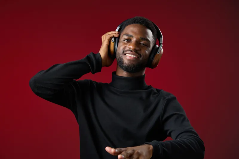 Happy young African man enjoying music with headphones in a stylish black turtleneck, set against a vibrant red background, conveying joy and energy