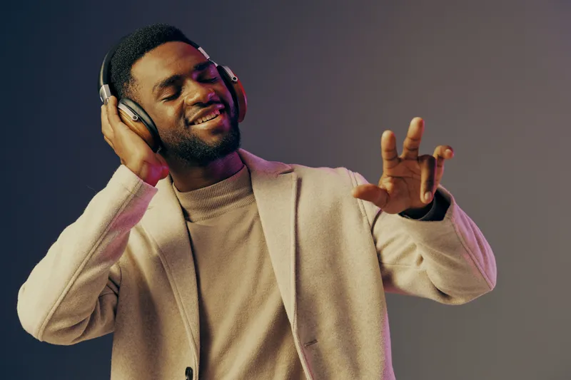 Young man enjoying music with headphones, smiling, dressed in stylish sweater, showcasing vibrant emotions in a colorful background