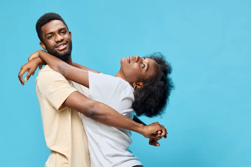 Happy couple expressing love and joy, wearing casual clothing against a blue background, showcasing emotions of affection and playfulness
