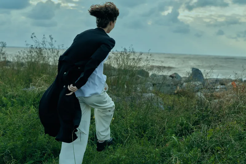 Dynamic figure in business attire runs along a grassy coastal path, wind-swept scene portraying ambition, journey and persistence toward a distant horizon