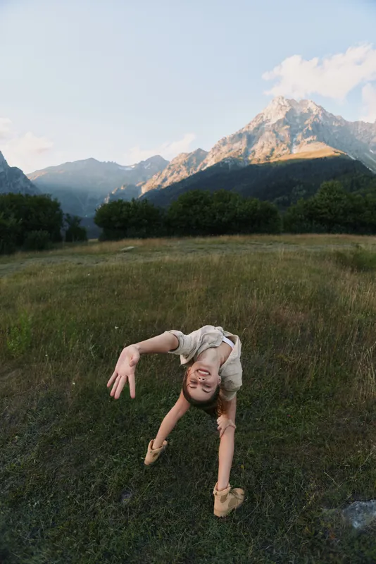 A woman performs a backbend in a grassy field with mountains in the background, capturing a spontaneous outdoor workout moment and a sense of freedom.