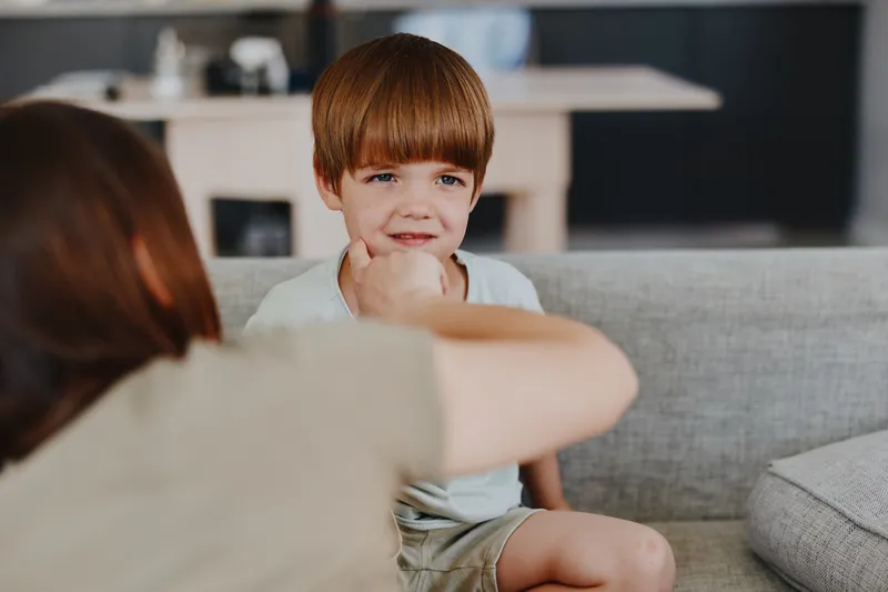 Smiling woman playing with her son, creating a joyful moment indoors. The soft lighting enhances the warmth and connection between them.