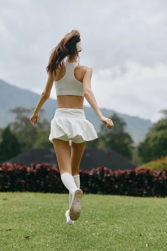 Young athletic woman in white sportswear running outdoors, showcasing an active lifestyle and fitness concept against a natural green background