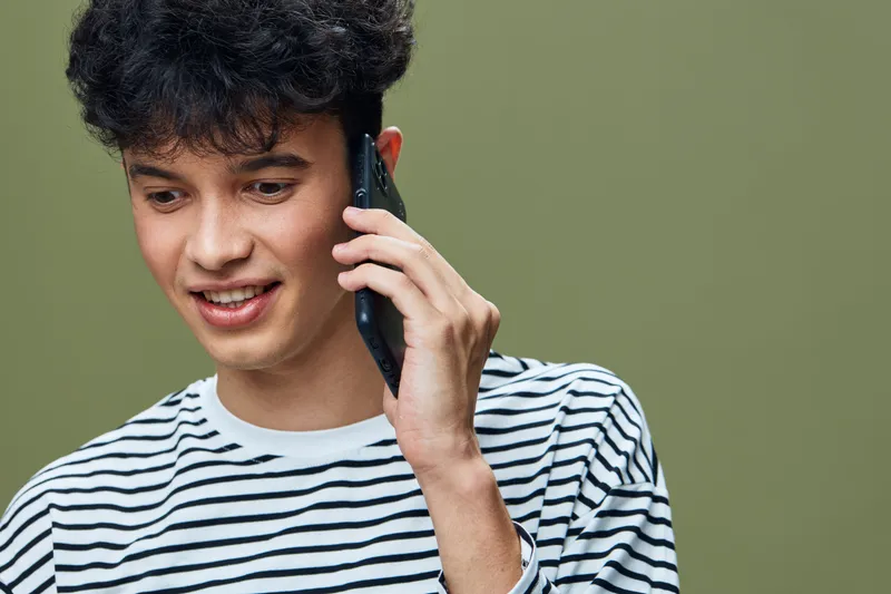 smiling man talking on smartphone wearing striped shirt with curly dark hair, casual communication, modern lifestyle, green background, young adult