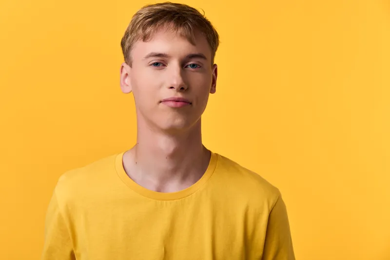 Young man in a yellow shirt in a bright studio, calm expression, clean background, suitable for fashion and lifestyle visuals with a simple headshot style