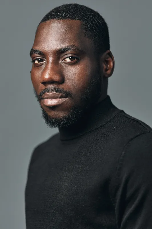 Portrait of African American man with dark skin and short hair wearing black turtleneck sweater looking at camera with confident expression in studio with neutral background.