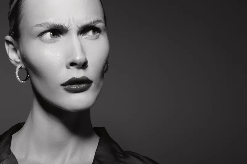 Portrait of a serious white woman with pale skin and short hair looking to the side. Studio lighting highlights her sharp features and contemplative expression. Concept of focus and thought.