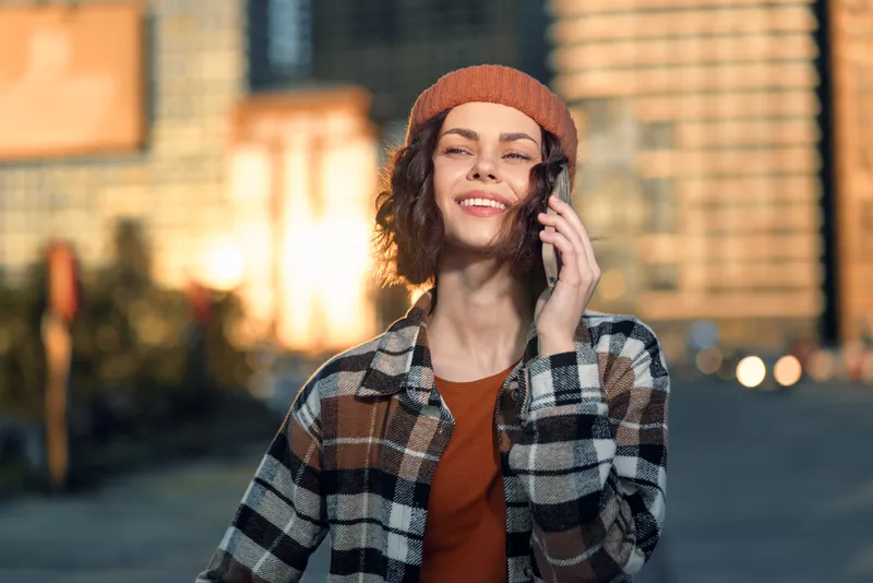 smiling woman phone city golden candid urban beanie captured in a candid lifestyle portrait, authenticity and mindful living at golden hour glow, emotional storytelling in modern street