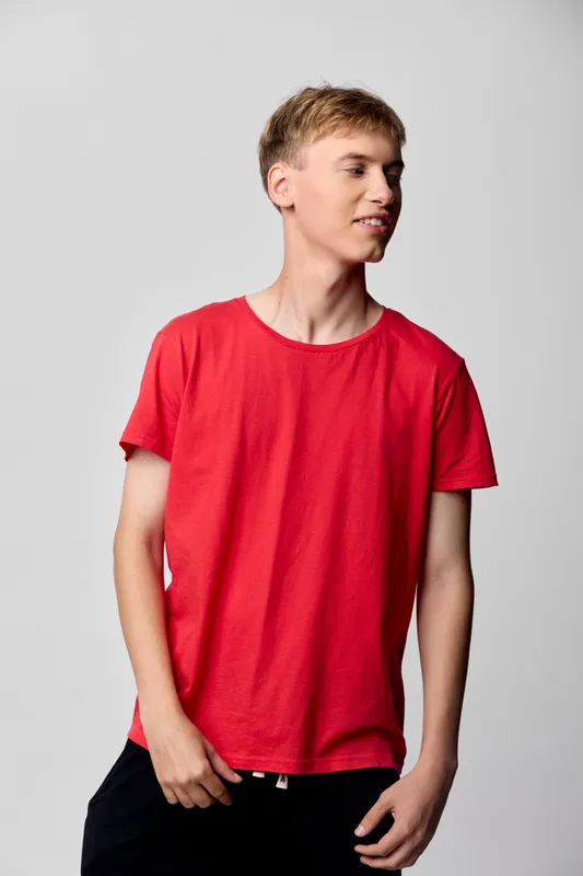 Red t shirt worn by young man in casual pose, standing in studio with bright lighting, simple background, relaxed expression, everyday fashion vibe, ideal for lifestyle and fashion stock use