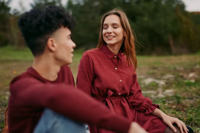 Young couple share a candid outdoor moment with genuine smiles and relaxed posture, capturing authenticity and credibility in a simple everyday connection bathed in soft natural light.