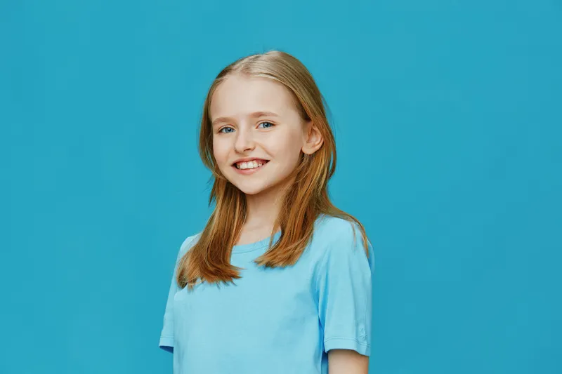 Happy girl with blonde hair smiling in a blue t shirt against a turquoise background, capturing joy and innocence, ideal for family and children related content