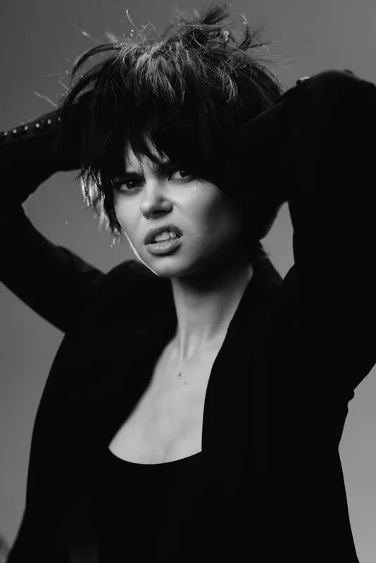Black and white portrait of a young woman with short hair in a moody expression wearing dark clothing