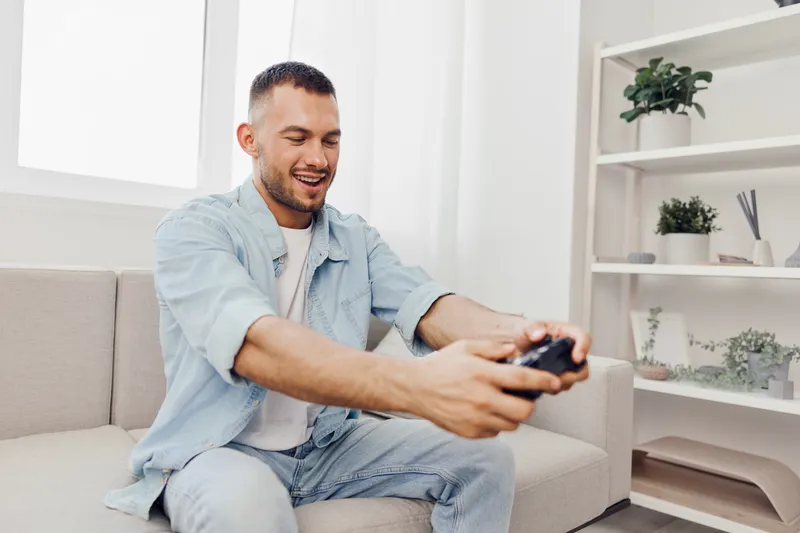 Engaged man playing video games at home, enjoying a digital escape while balancing work-life dynamics and personal well-being, in a cozy living room setting.