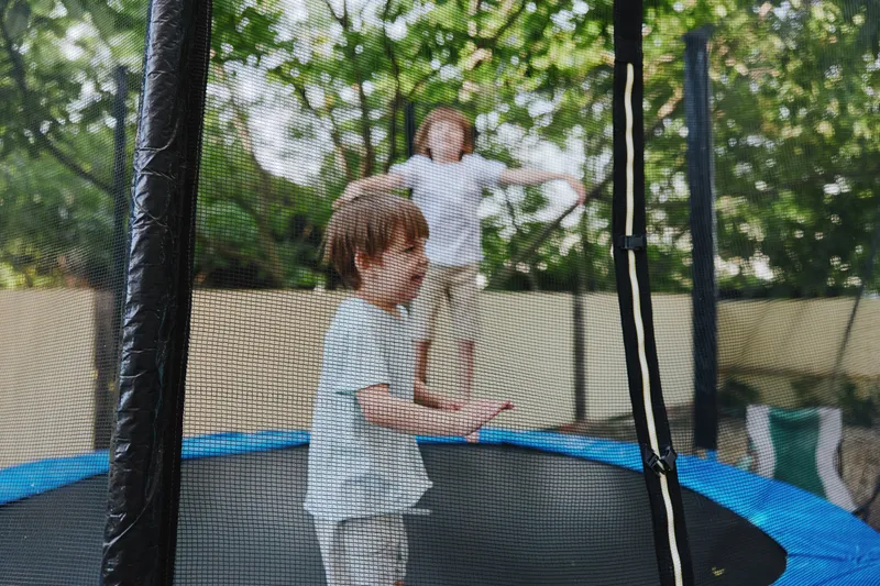 Happy children jumping on a trampoline in a sunny backyard, showcasing pure joy and playful energy amidst a lush green backdrop. ###