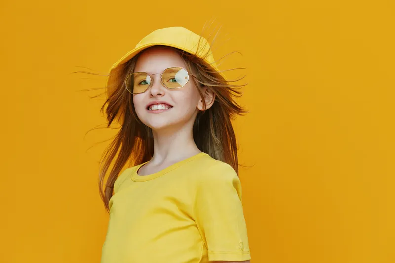Cheerful girl in yellow outfit and sunglasses smiles against a vibrant yellow background, showcasing summer joy and playful energy, perfect for cheerful themes