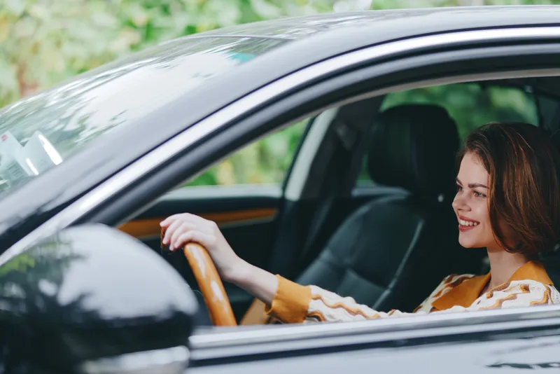 Smiling woman behind the wheel of a car, relaxed pose in the driver's seat, capturing a confident driving moment.