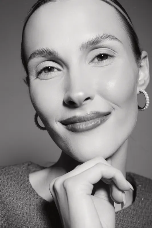 Close-up portrait of a smiling Caucasian woman with light skin and hoop earrings in monochrome. Concept of natural beauty and confidence.