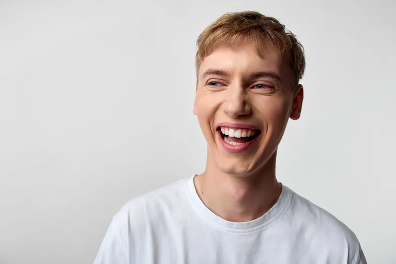Smiling man in a white casual shirt, expressing happiness and laughter in a clean studio, conveying warm energy, positive mood, and approachable charm for lifestyle, wellness, or happiness themes